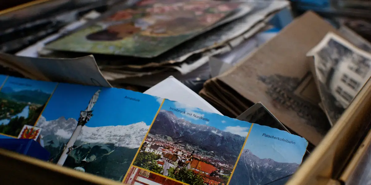 Cutie de carton deschisă, plină de cărți poștale austriece vechi; deasupra, una cu Innsbruck mit Nordkette și casete mai mici etichetate Annasaeule, Patscherkofelbahn și Hofkirche