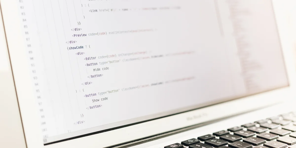 Ecranul unui laptop cu codul-sursă al unei pagini web: etichete HTML și fragmente de JavaScript la focus, tastatura în prim-plan