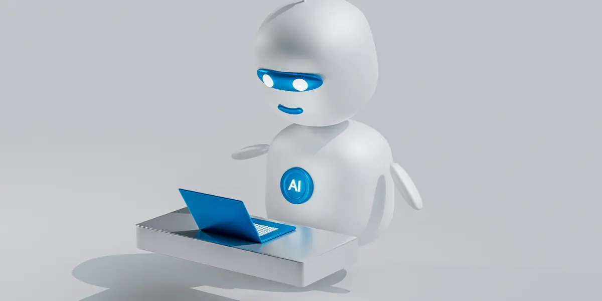 A stylised white robot with glowing blue eyes and a round badge reading AI on its chest, sitting in front of a miniature blue laptop on a light grey background