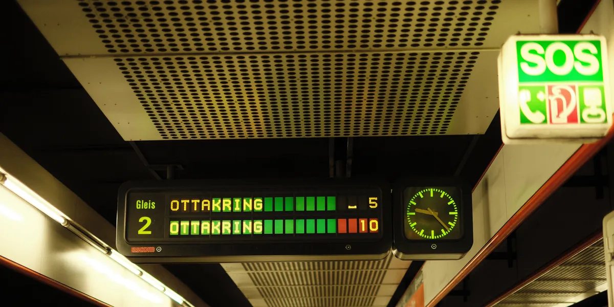 Panou de afișaj pe un peron de metrou din Viena, cu caractere galbene și verzi care arată destinația Ottakring și timpii de așteptare de 5 și 10 minute, lângă un indicator luminos SOS
