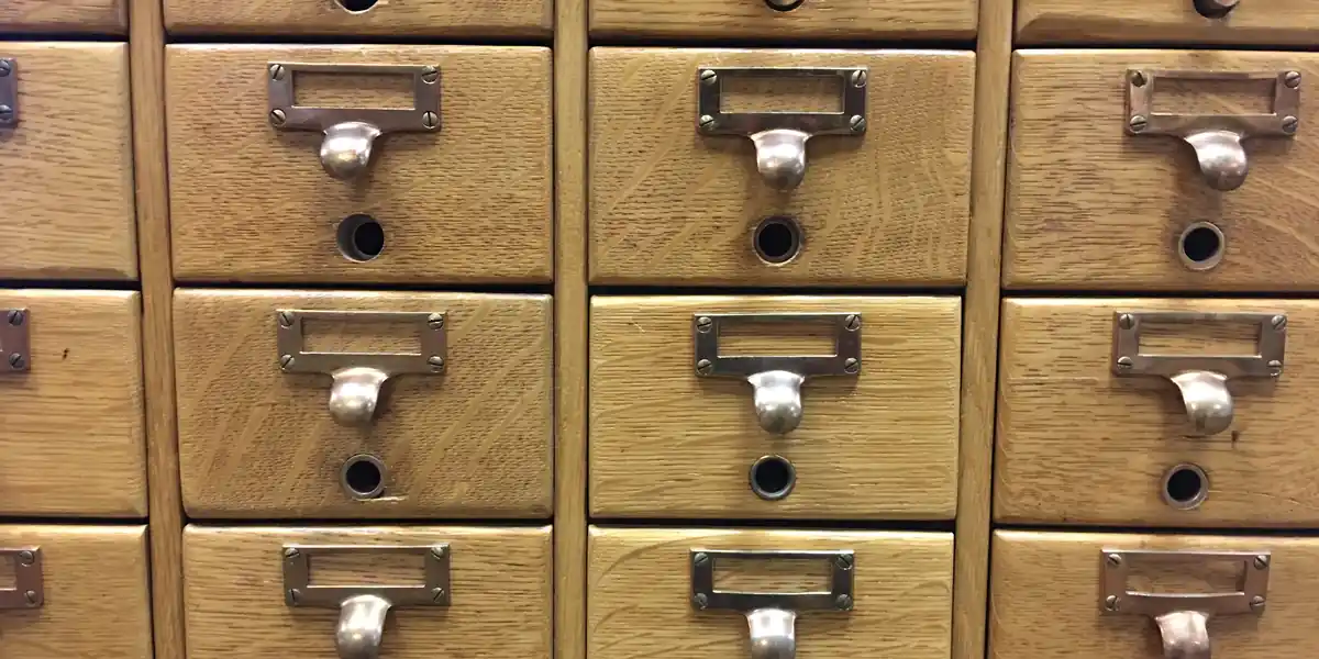 Grid of oak library catalogue drawers with brass pull handles and empty metal label holders on every drawer front